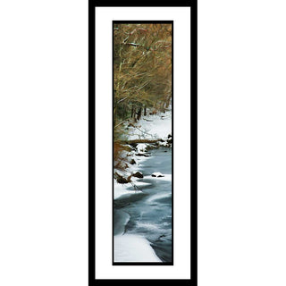 Bare trees line a winter stream, their whisper-thin branches making a web that shields the rest of the forest from view. Snow gathers on the riverbank and dusts the ice covering the water. Winter Stream by Alison Thomas of Serenity Scenes Photography and Digital Art